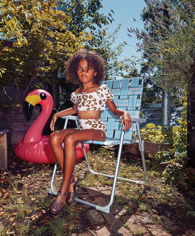 Child in a leopard-print bathing suit sitting on a lawn chair outdoors next to an inflatable pink flamingo on a sunny day.