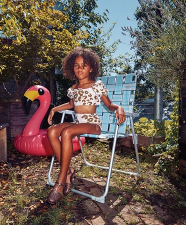 Child in a leopard-print bathing suit sitting on a lawn chair outdoors next to an inflatable pink flamingo on a sunny day.