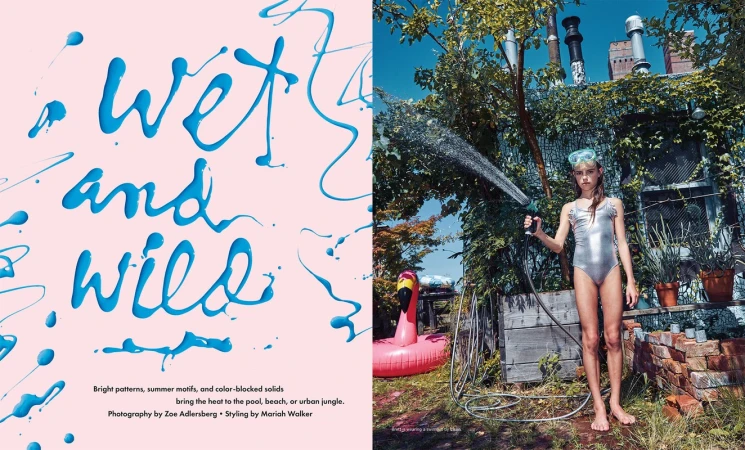 Young girl in swimsuit outside spraying a hose. Text overlay reads 'wet and wild'. Pink flamingo floatie and foliage in the yard.