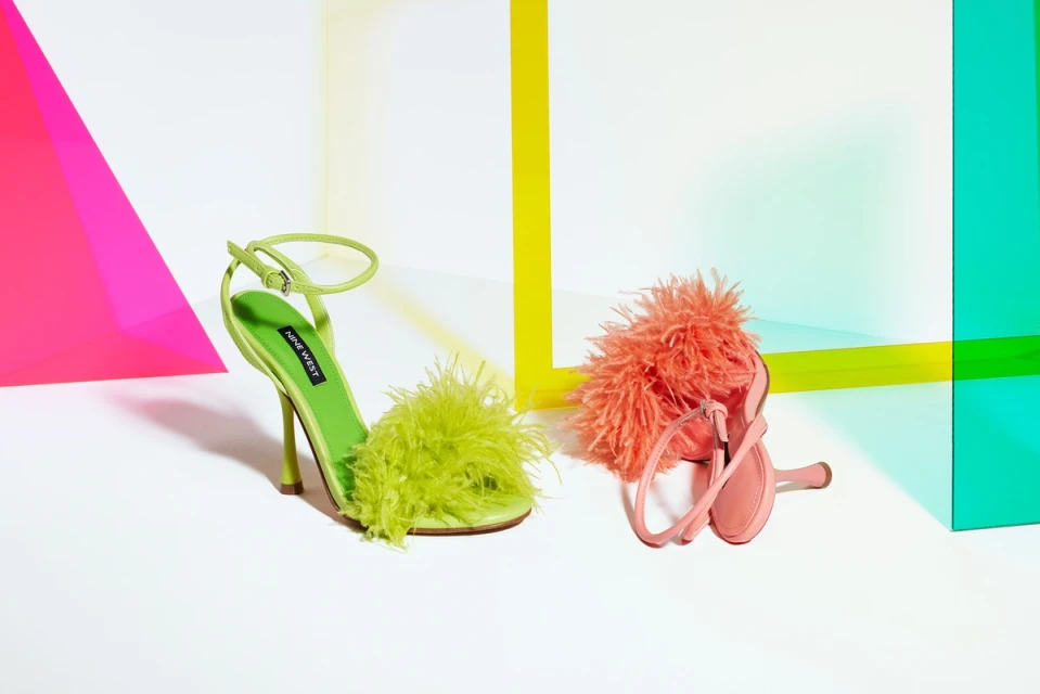 Two fashionable strappy high-heeled sandals with green and coral fluffy feather-like textures, set against a colorful geometric background.