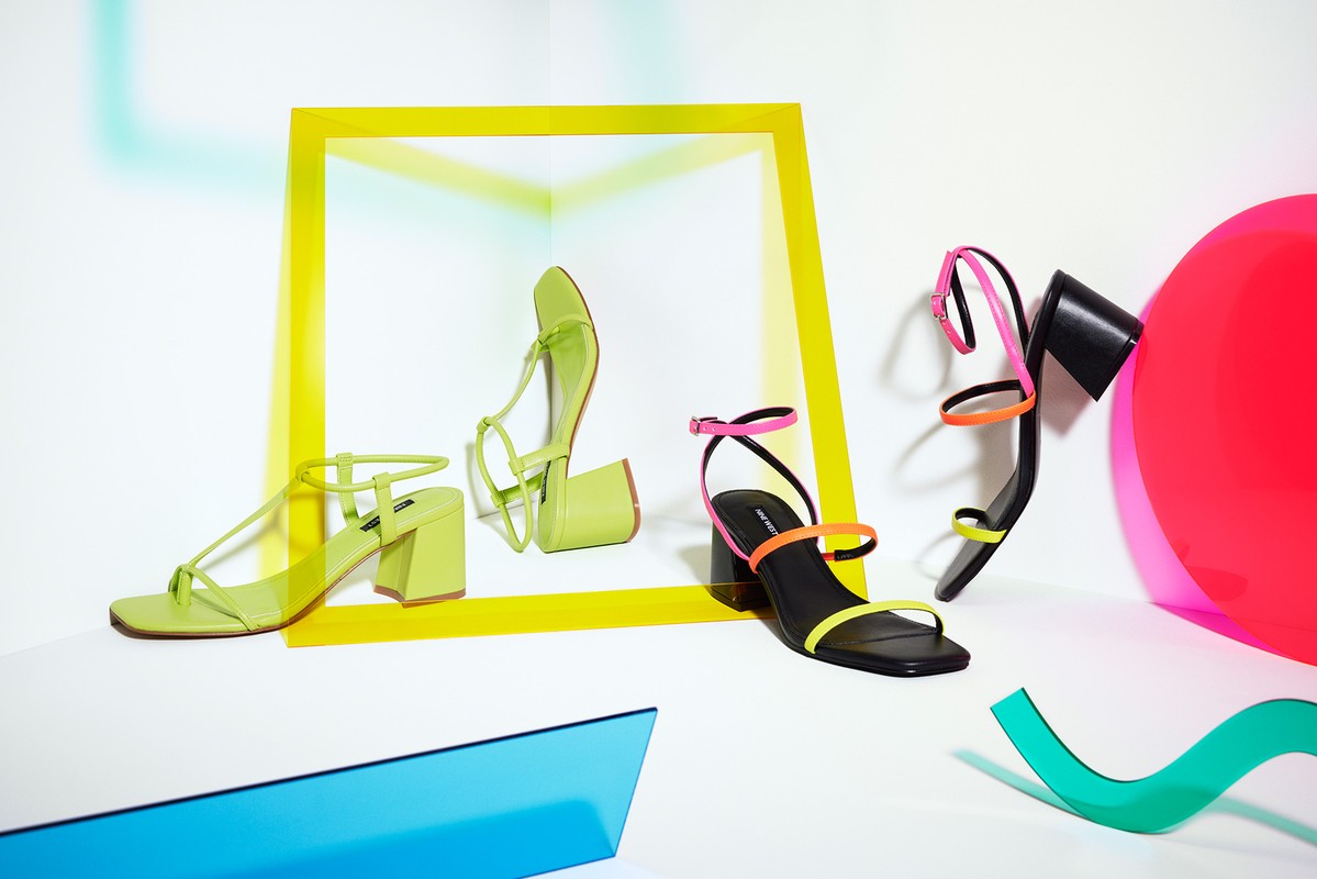 Stylish strappy heeled sandals in bright neon colors arranged creatively with geometric props and studio lighting for a fashion editorial.