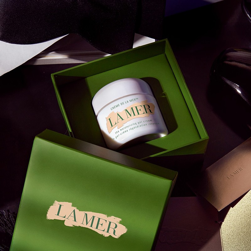 La Mer cream in a green branded box on a dark surface surrounded by dark accessories creates a beauty and luxury product scene.