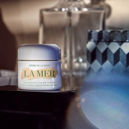 Close-up studio shot of a white jar of La Mer moisturizing gel cream against a blurred background with decorative objects.