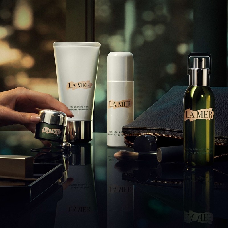 La Mer skincare product set featuring creams, serums, and cleansers in a luxury beauty flat lay arrangement with hand interaction.