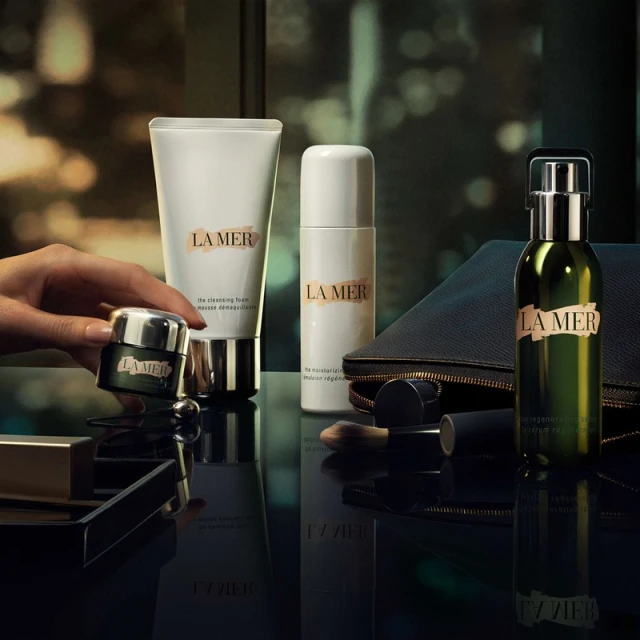 La Mer skincare product set featuring creams, serums, and cleansers in a luxury beauty flat lay arrangement with hand interaction.