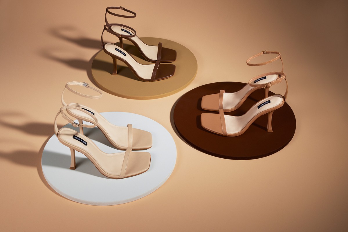 Studio product shot of three pairs of Nine West stiletto heels in white, beige and brown tones, arranged on matching circular platforms.