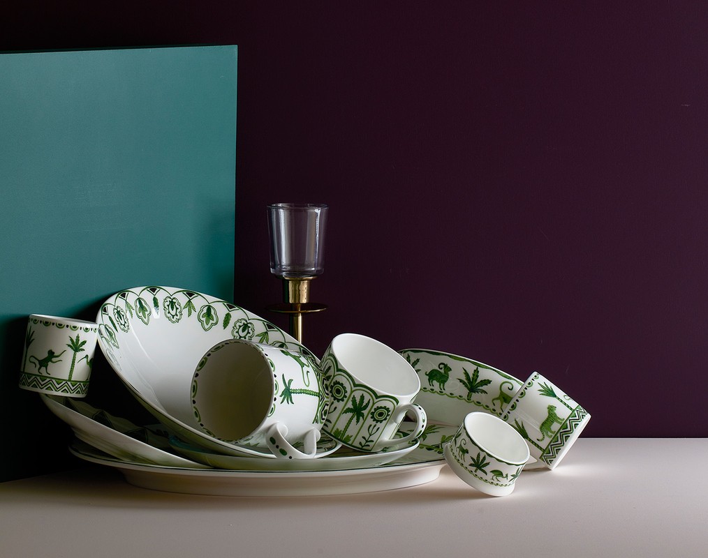 Arrangement of white ceramic tableware with green foliage and animal pattern designs, set against teal and dark purple backdrop.