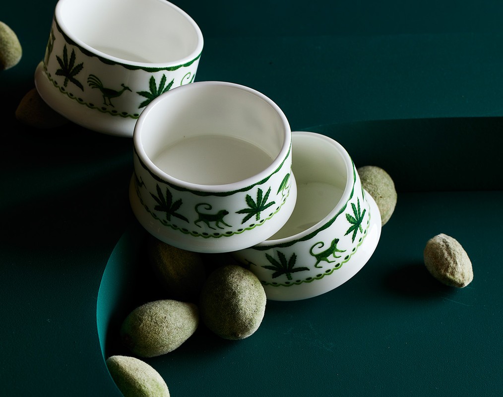 Overhead shot of three white ceramic bowls with green decorative trim, interspersed with green felted balls on a dark green surface.