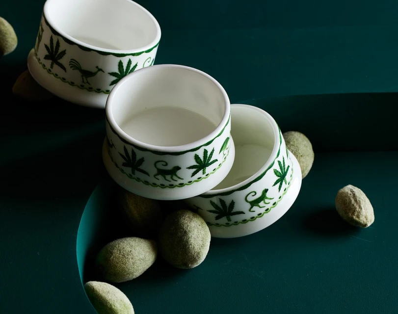 Overhead shot of three white ceramic bowls with green decorative trim, interspersed with green felted balls on a dark green surface.
