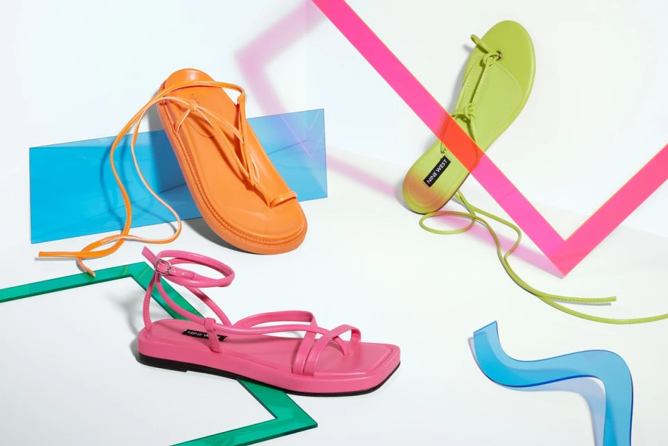 Three colorful Nine West sandals, including orange, pink, and lime-green. Flat lay with geometric shape props on a white backdrop.