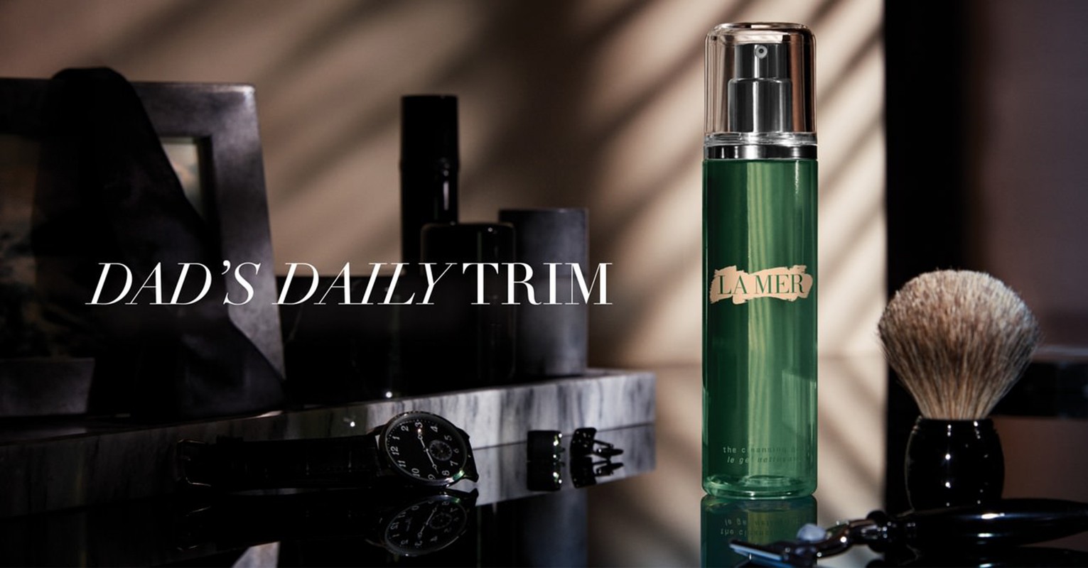 Close-up of grooming products by La Mer, including shaving brush, serum, and razor, displayed on a polished marble surface.
