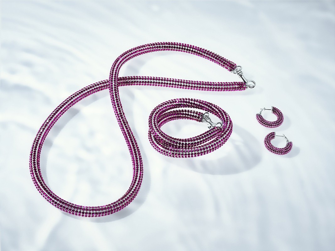 Elegant jewellery set on a white surface with soft lighting: necklace, bracelet, and pair of earrings with pink gemstones.