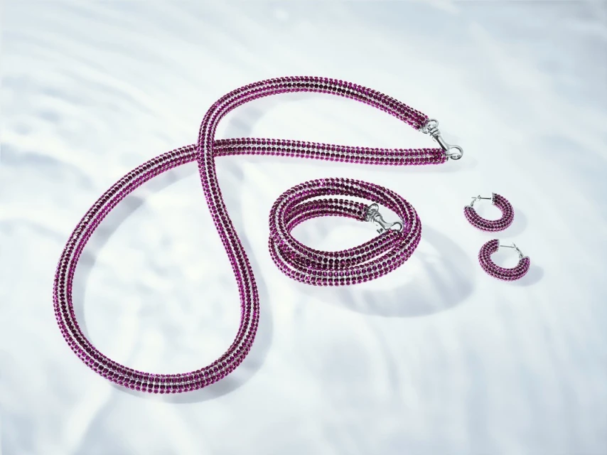 Elegant jewellery set on a white surface with soft lighting: necklace, bracelet, and pair of earrings with pink gemstones.