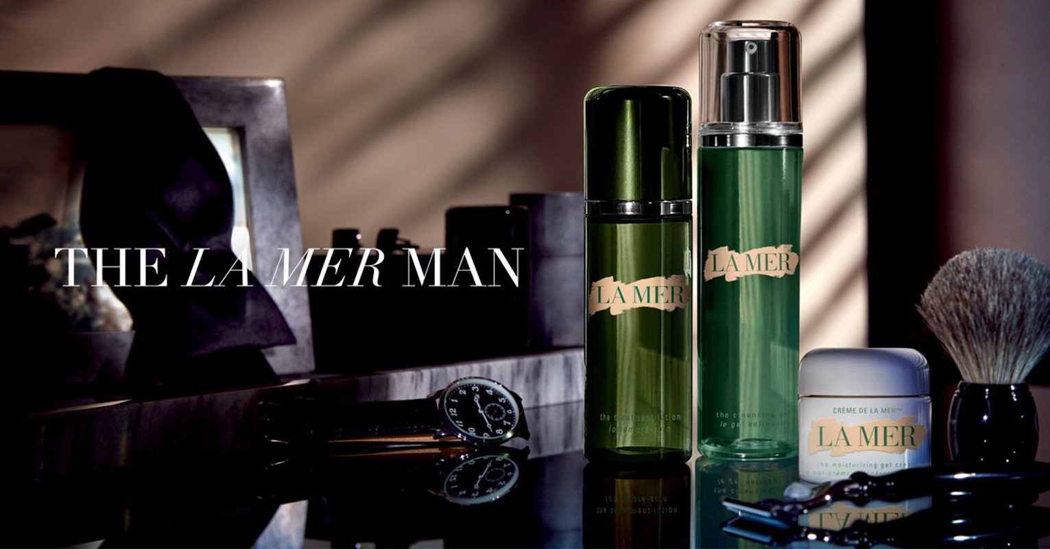 La Mer men's skincare product line arranged on a reflective surface. The image includes shaving brush, razor, and a watch.
