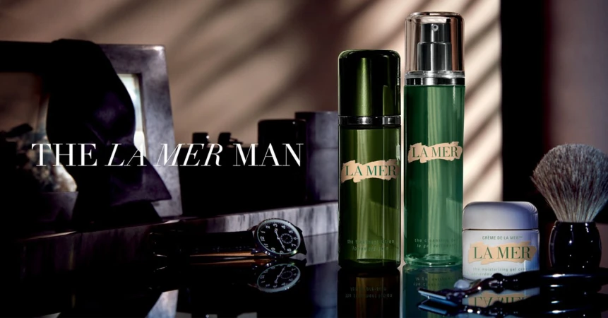 La Mer men's skincare product line arranged on a reflective surface. The image includes shaving brush, razor, and a watch.