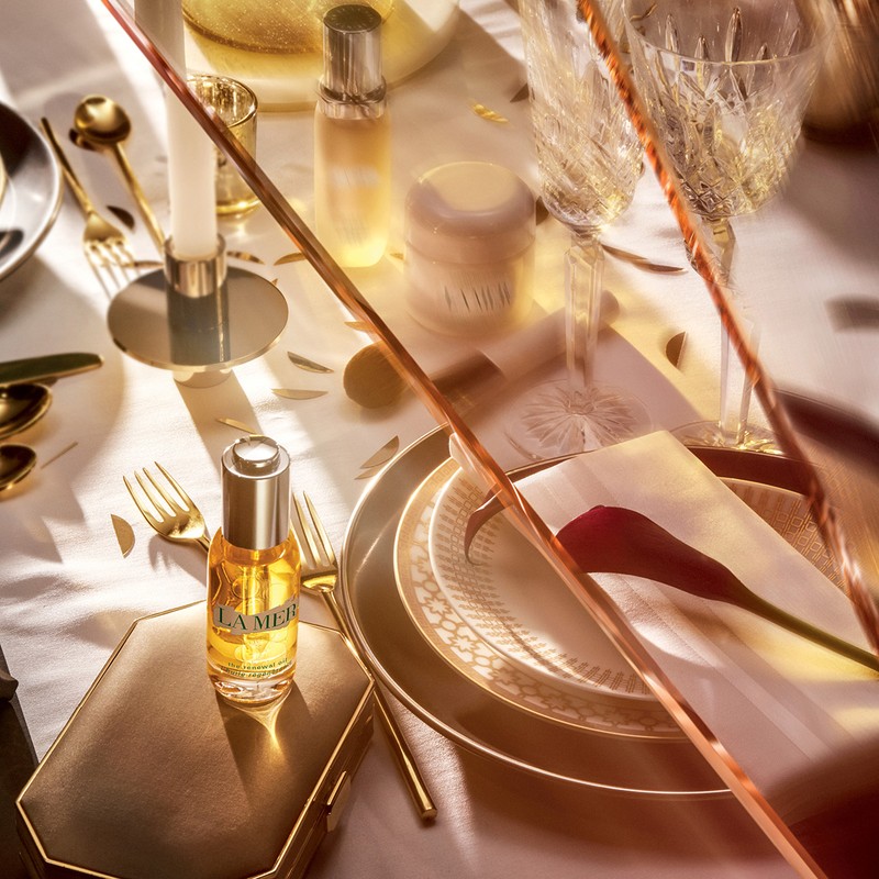 Overhead shot of La Mer skincare products amidst an elegant table setting with golden flatware, plates, glasses and decorations.