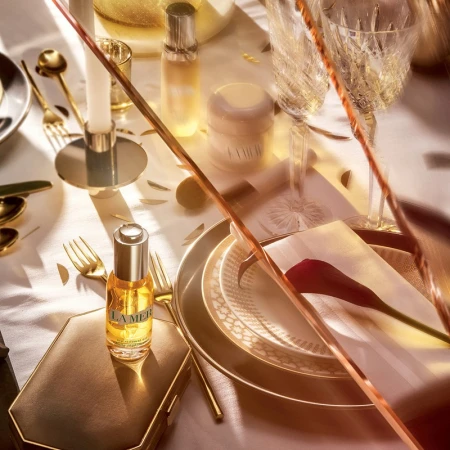 Overhead shot of La Mer skincare products amidst an elegant table setting with golden flatware, plates, glasses and decorations.
