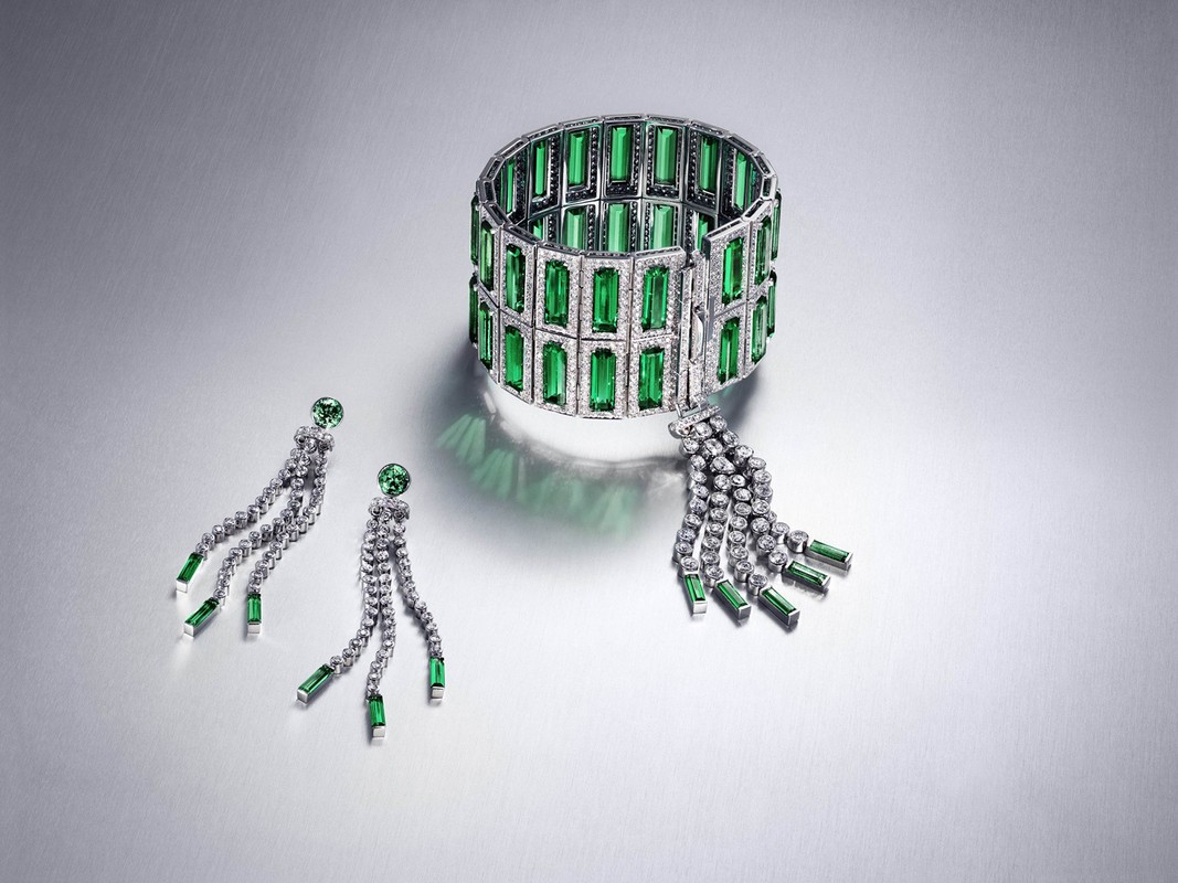 Elegant green emerald and diamond jewelry set featuring a bracelet and earrings, displayed on a grey gradient background in a studio shot.