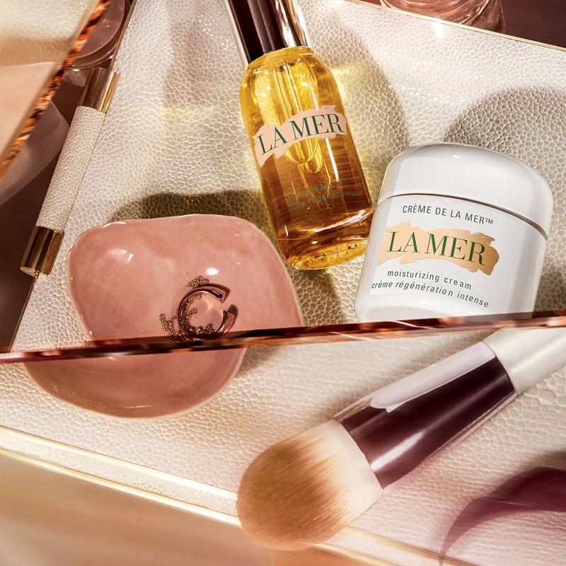 Close-up of La Mer skincare products including moisturizing cream, oil, makeup brush, and applicator on a cosmetic tray.