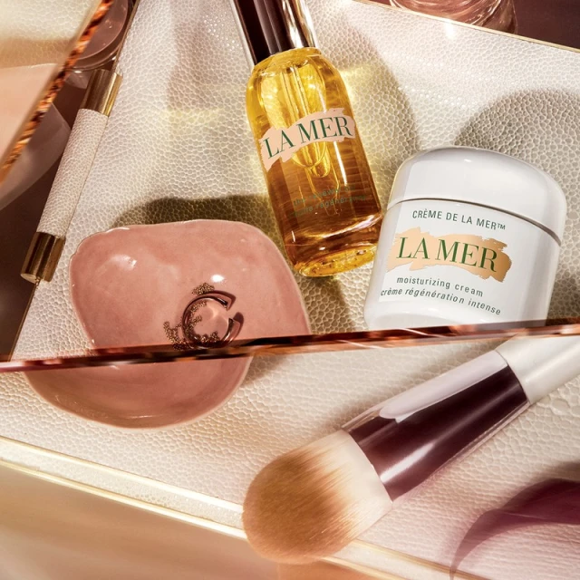 Close-up of La Mer skincare products including moisturizing cream, oil, makeup brush, and applicator on a cosmetic tray.
