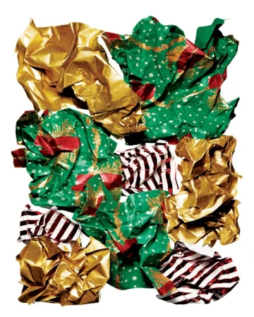 Crushed and crumpled gold and green patterned wrapping paper, discarded on a white surface, suggesting festive waste.