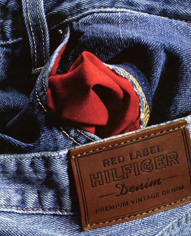 Close-up studio shot of blue denim jeans with a brown leather label, showcasing a red fabric detail in the pocket.
