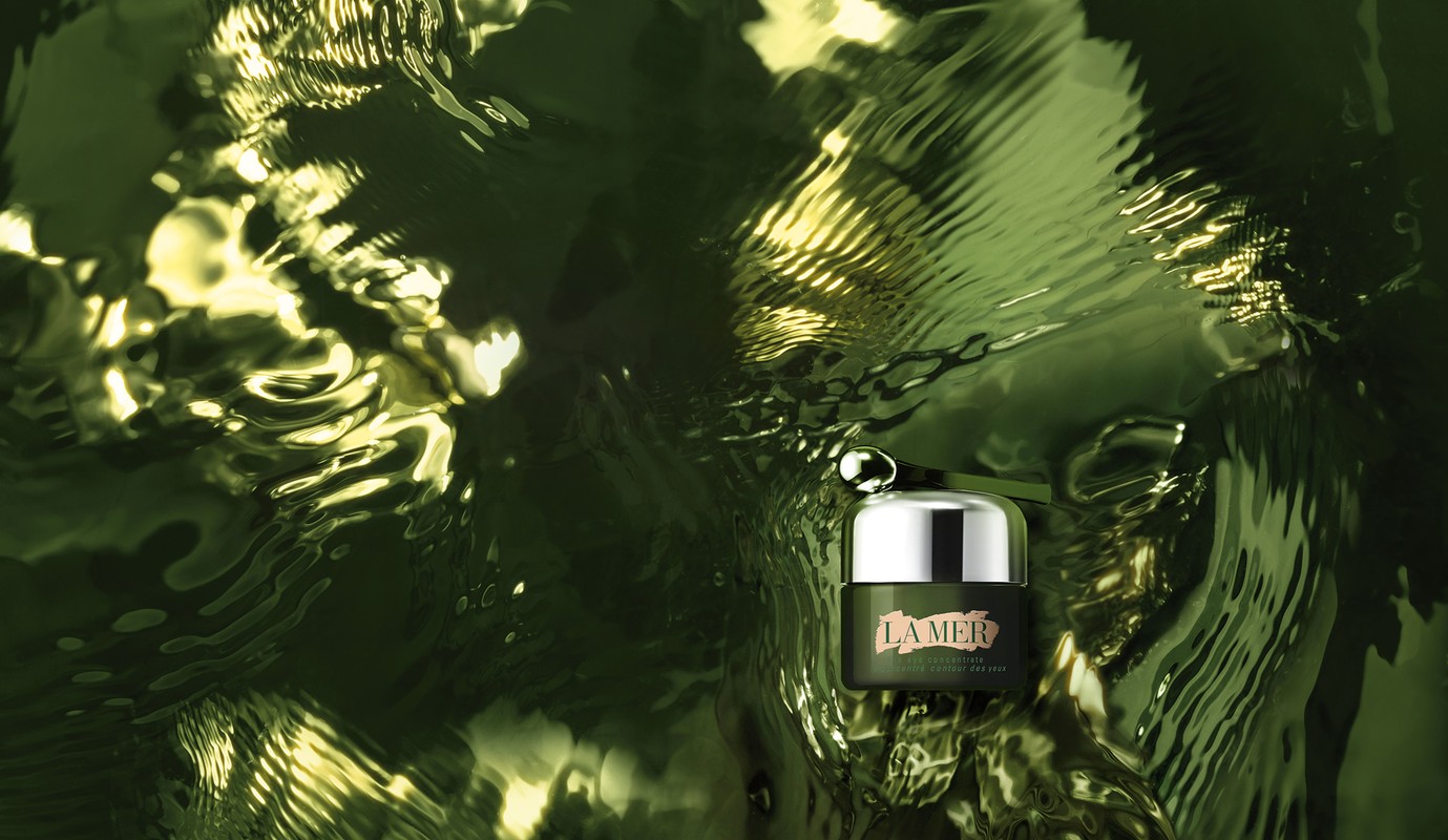 La Mer skin cream jar with applicator shown in studio setting over a reflective surface. Skincare advertisement shot, beauty product.