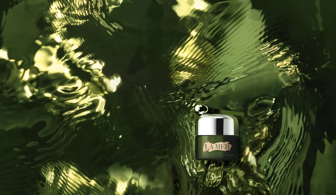 La Mer skin cream jar with applicator shown in studio setting over a reflective surface. Skincare advertisement shot, beauty product.