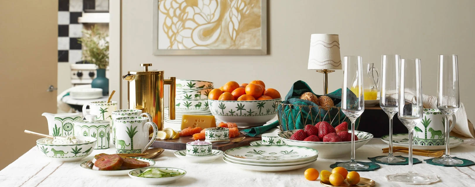 Table setting with fresh fruit, brass accents, and elegant white and green patterned dishware creates a bright, inviting atmosphere.