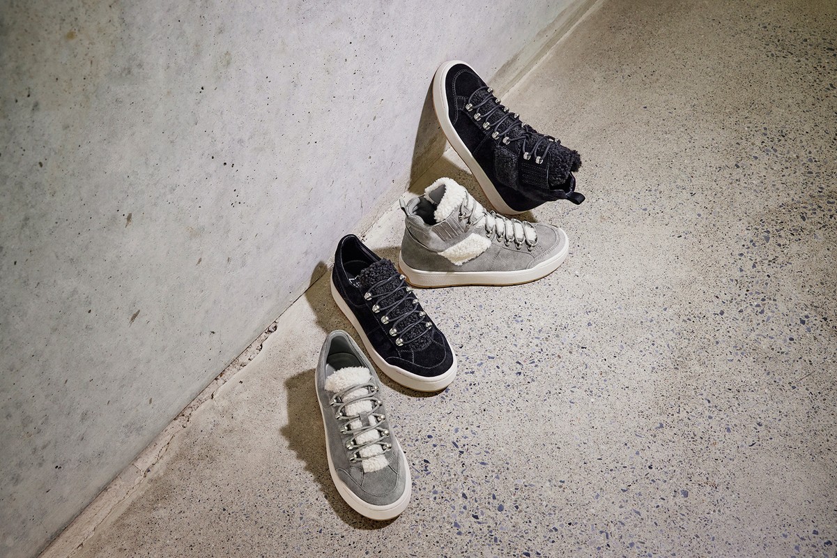 Two pairs of stylish grey and black lace-up shoes displayed on a grey textured surface, casting soft shadows with indoor lighting.