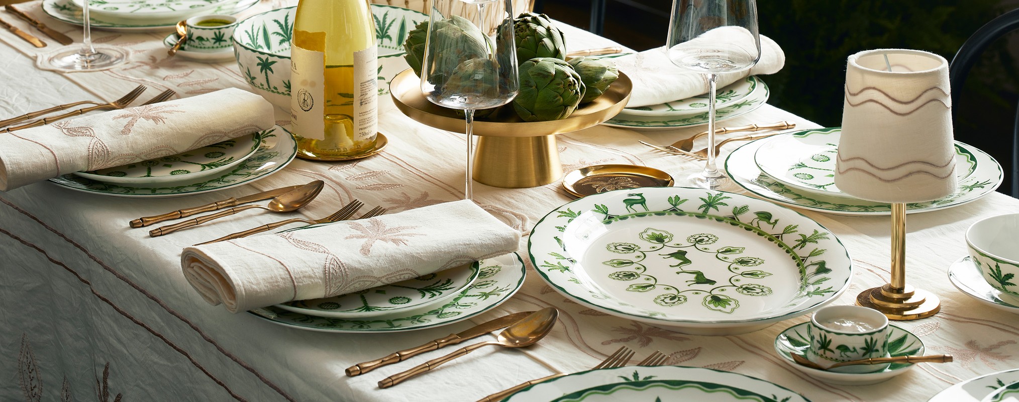 An elegantly set table features patterned china, gold flatware, crystal glassware, and decorative accents, creating a refined dining atmosphere.