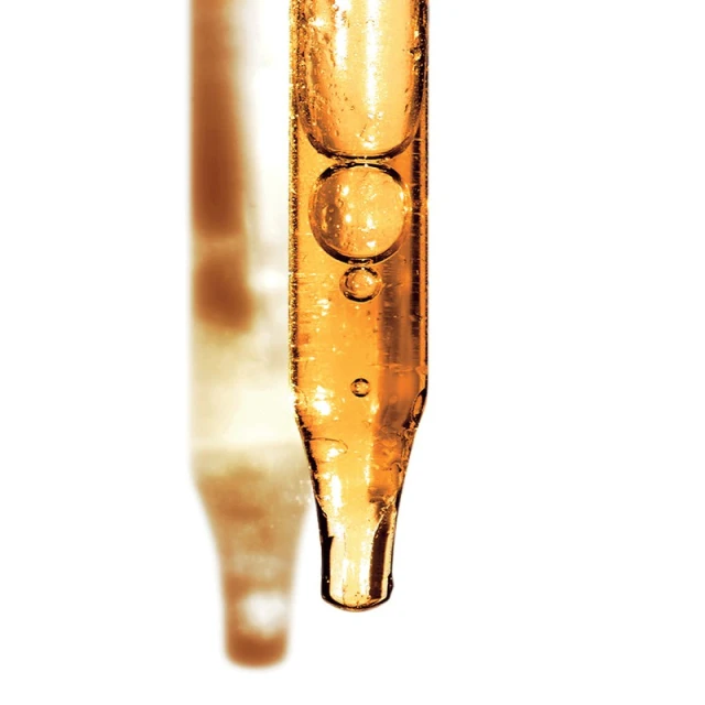Close-up of a pipette filled with golden liquid, showcasing its transparent body, the bubbles within, and a blurred reflection.
