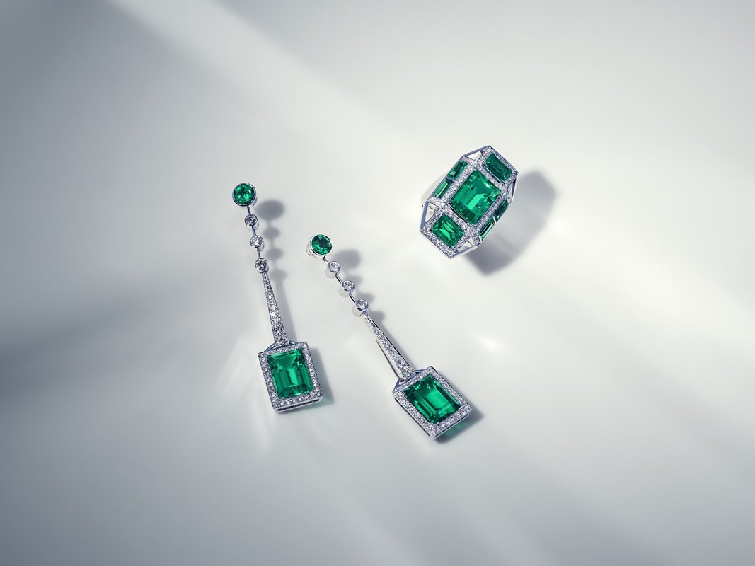 Elegant emerald and diamond jewelry set featuring a ring and drop earrings, arranged on a soft, illuminated white surface. Jewelry photography.