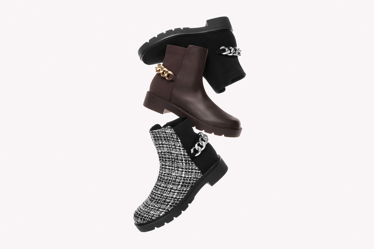 Three fashionable ankle boots are stacked against a white backdrop, each with distinctive textures, brown and black tones, and chain embellishments.