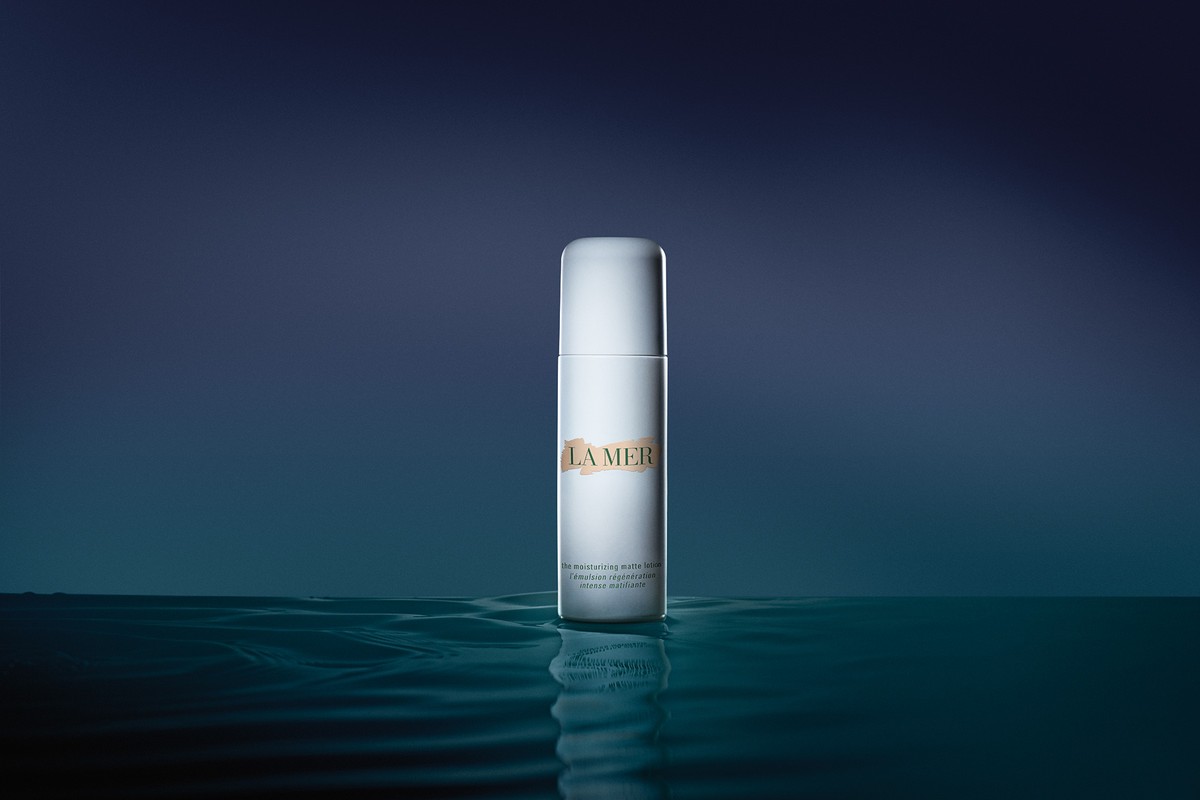 LA MER skincare product bottle in a minimalist dark blue beauty product studio shot, focus on the bottle with water reflection.