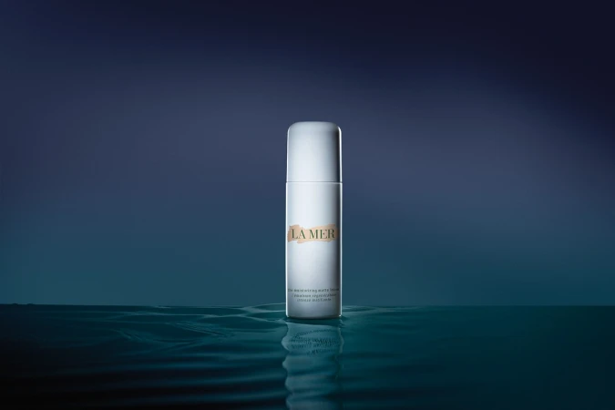 LA MER skincare product bottle in a minimalist dark blue beauty product studio shot, focus on the bottle with water reflection.
