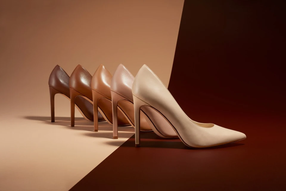 Elegant arrangement of brown, tan, and beige high heel shoes in a studio setting with a contrasting two-tone background.