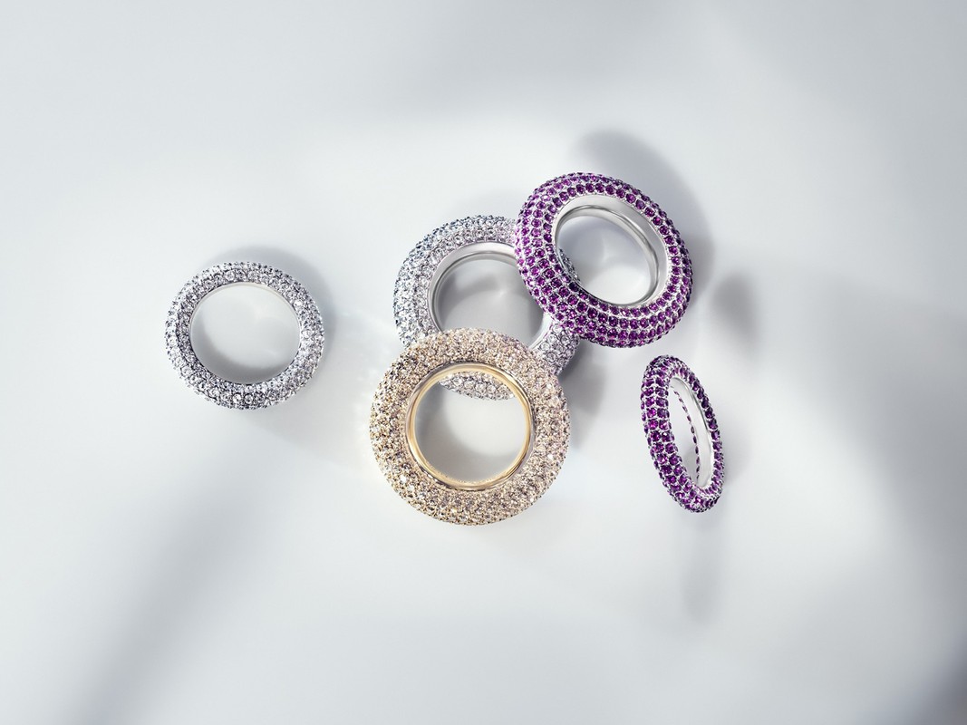 Several jeweled rings in silver, gold, and purple tones are arranged on a gradient white backdrop with soft, diffused lighting.