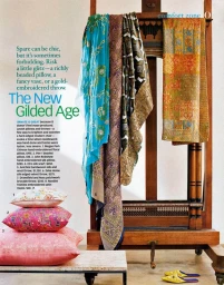 Decorative pillows, draped colorful textiles, and yellow mules styled on a wooden rack and stone bench with magazine article text