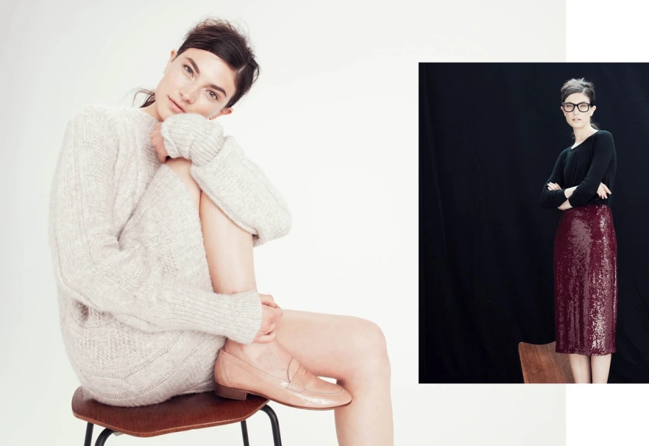 Two women in a fashion setting. One sits wearing a sweater and loafers, the other stands with crossed arms in a skirt and top.
