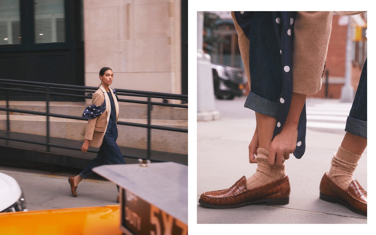 A stylish woman in a tan blazer walks in an urban setting near a yellow taxi. Close-up on brown loafer shoes with beige socks and rolled denim.