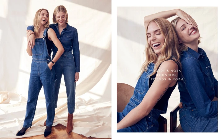Two blonde women wearing denim clothing pose in a bright studio. One wears overalls and a top, while the other wears a denim shirt and jeans.