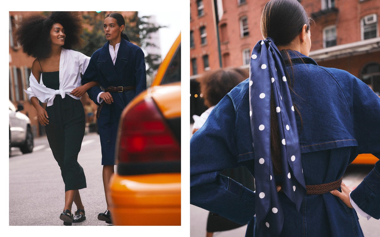 Two women in fashionable clothing walk on a city street with a yellow taxi cab. One woman wears a white blouse and black pants.