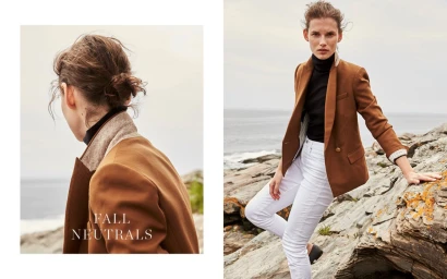 Model in a brown blazer and white trousers posing on a rocky coastal shore with an ocean background.