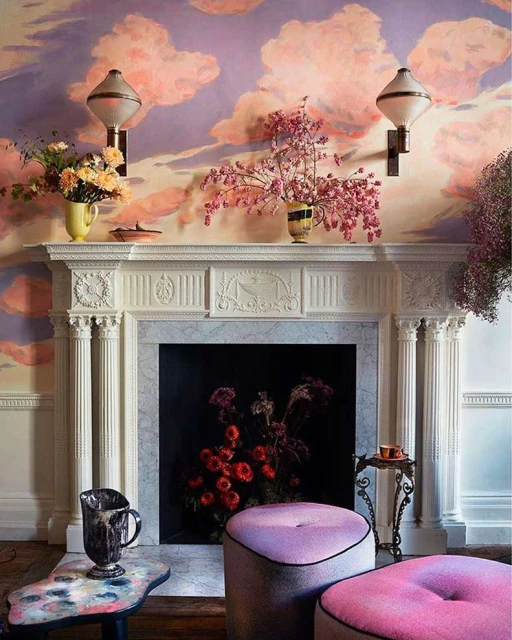 Living room featuring a white fireplace decorated with floral arrangements, sconces, and cloud-patterned wallpaper.