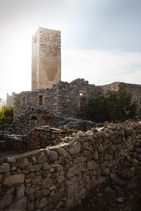 Stone ruins in rural setting under bright sky. An old, tall stone tower stands amid the weathered, crumbling stone architecture.