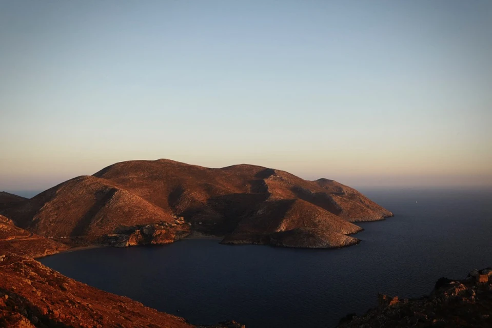 Hills and mountains meet the sea under a clear sky with golden light during daytime, creating a serene landscape.
