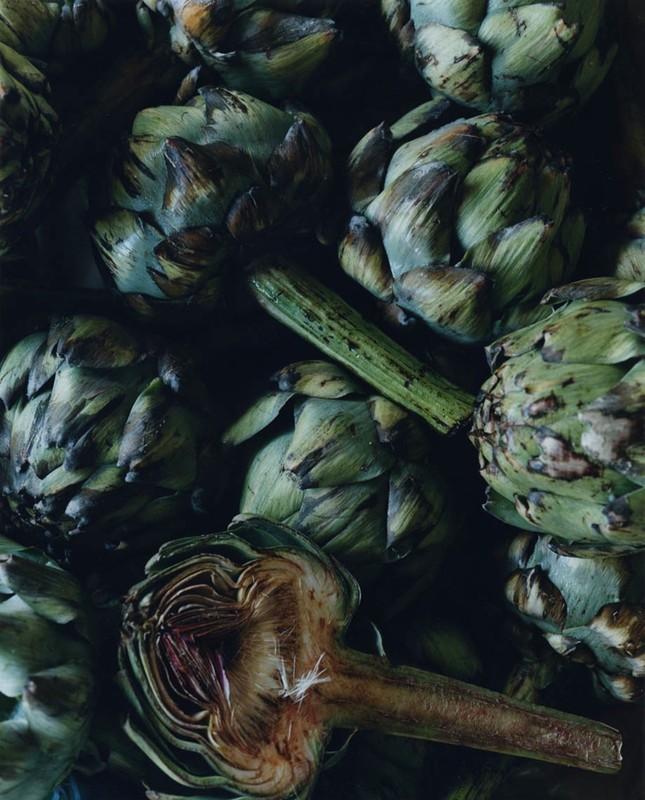 Overhead shot showcasing a pile of green artichokes and one cut open, revealing its interior with a visible stem.