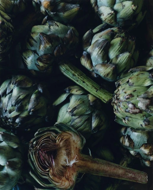 Overhead shot showcasing a pile of green artichokes and one cut open, revealing its interior with a visible stem.