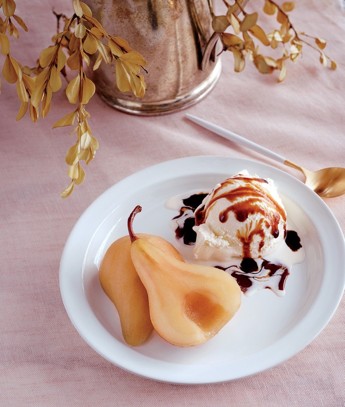 Poached pears served with vanilla ice cream and caramel sauce, plated on a white plate with a silver pitcher in the background.